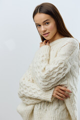 Wall Mural - a beautiful, attractive, relaxed woman stands touching her neck with her fingers in a white knitted sweater and gently looks at the camera