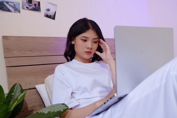 Wall Mural - Serious young woman sitting in bed when working on laptop at late night