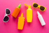 Fototapeta Kawa jest smaczna - Top view of sunglasses and bottles of sunscreens on pink surface.