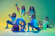 Leinwandbild Motiv Group of children, little girls in sportive casual style clothes dancing in choreography class isolated on green background in yellow neon light. Concept of music, fashion, art