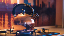 Close-up Of Silver Teapot Boiling On Stove. Concept. Boiling Kettle On Stove In Beautiful Evening Kitchen Interior. Stream Of Steam Comes Out Of Kettle On Stove