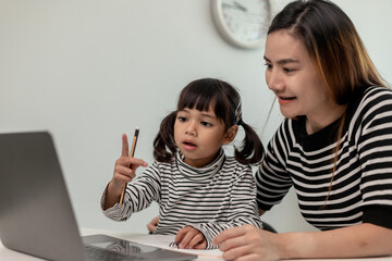 Asian little young girl kid learning online class at home with mother. Preschool child use laptop computer do homework, homeschool from school teacher by digital remote internet with support from mom.