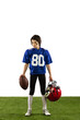 © master1305 - One sportive boy, american football player in blue sports uniform and protective equipment posing isolated on white background with green grass flooring.