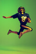 © master1305 - Sportive little boy in sports uniform and equipment playing american football isolated on green background in neon light. Concept of sport, movement, achievements.