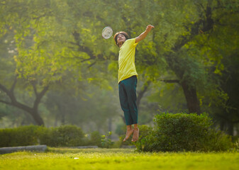 Wall Mural - Handsome young indian man playing badminton in the park. urban asian sporty male having fun outdoor sports and game activity concept.