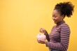 © Chalermphon - Young African american woman with a piggy bank on a pink background.Beautiful female with black afro hair holding coin to Saving piggy bank.