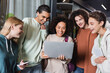 © LIGHTFIELD STUDIOS - happy african american woman holding laptop near smiling multiethnic friends.