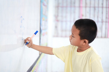 Asian kid doing multiplication math on white board in learning activity