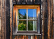 altes Fenster eine Almhütte mit einem Blumenstrauß und Spiegelungen der Berge im Fenster