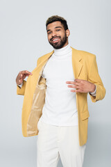 Wall Mural - cheerful african american man adjusting yellow blazer isolated on grey.