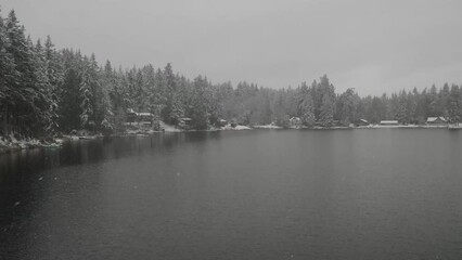 Wall Mural - Floating over a lake in winter with the snow falling and calm water.