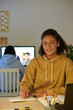 © DragonImages - Smiling high school student doing homework when her sister ha Indian online class in background