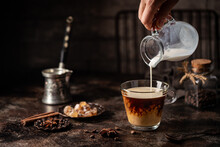 Coffee In A Glass With Cream Poured Over, Sugar And Coffee Beans On Dark Background