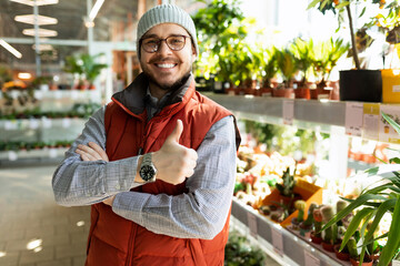 a sales assistant in a gardening goods store looks at the camera with a smile and shows a like symbol