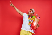 Excited Young Man In Hawaiian Necklace Carrying Inflatable Cocktail Glass And Pointing Away