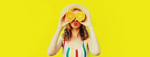 Summer Portrait Of Cheerful Young Woman Covering Her Eyes With Slices Of Orange Fruits And Looking For Something Wearing Straw Hat On Yellow Background
