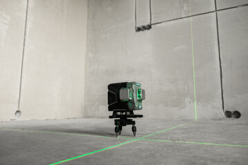 Laser level, construction, finishing work in the room. Laser building level with green beams on the wall bare cement of the house