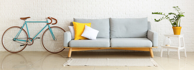 Grey sofa, stepladder with houseplant and bicycle near white brick wall