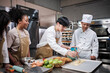 Cuisine course, senior male chef in uniform teaches young cooking class students, brushes pastry dough with eggs cream, prepares ingredients for bakery foods, fruit pies in stainless steel kitchen.