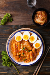 Wall Mural - Korean spicy instant noodle with Tteokbokki, sausage and egg on wooden background, Table top view