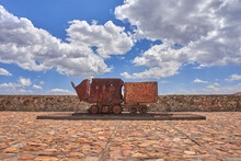 Old Rusty Mining Cart On An Ornamental Track In A Stone Yard With A Blue Sky With Clouds In The Background On A Sunny Summer Day