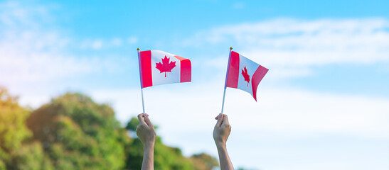 Wall Mural - hand holding Canada flag on blue sky background. Canada Day  and happy celebration concepts