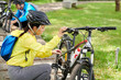 © DragonImages - Asian young woman in bicycle helmet checking wheels and tires before ride