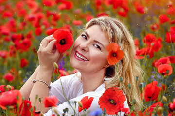 Wall Mural - Stunning close portrait of a young blonde Caucasian woman with a poppy flower near her face. Happiness. Beauty and fashion concept