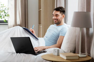 Sticker - people, technology and remote job concept - man with laptop computer and clipboard working in bed at home bedroom