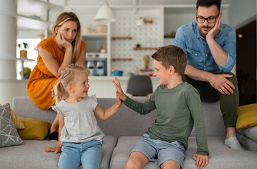 Tired parents sitting on couch feels annoyed exhausted while happy children playing together.