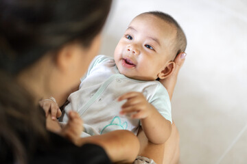 Portrait of enjoy happy love family asian mother playing with adorable little asian baby.Mom touching with cute son moments good time in a white bedroom.Love of family concept.