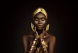 © kharchenkoirina - Portrait closeup Beauty fantasy african woman face in gold paint. Golden shiny black skin. Fashion model girl goddess hand fingers posing. Arab turban jewellery bracelets. Professional metallic makeup