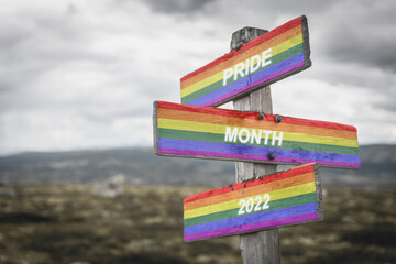 pride month 20222 text on wooden signpost with lgbtq flag outdoors in nature. Equality and freedom concept.