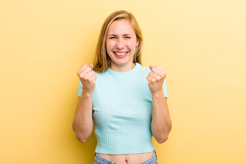 young adult  blonde woman shouting triumphantly, laughing and feeling happy and excited while celebrating success