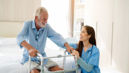 Care worker helping elderly man get out of bed and walk around the room.