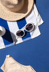 Wall Mural - Summer vacation beach concept frame with retro sunglasses, striped towel and straw hat on the blue background. Copy space 