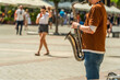 A street musician plays the saxophone on a sunny day on the street of a European city in front of passers-by walking in a European city on a summer day in Krakow, Poland