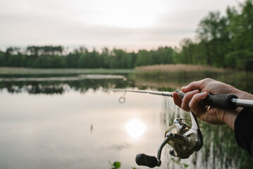 Wall Mural - Fisherman with fishing rod, spinning reel on the background river bank. Sunrise. Fishing the backdrop of lake.