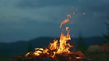 Campfire At Dusk Against The Backdrop Of Mountains And Forest. Tourist Bonfire With Sparks Flying In The Air, Slow Motion Shot.