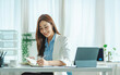 © Phushutter - Young Asian woman sitting at a table and writing notes. Businesswoman working at her desk.