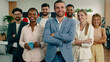 © spoialabrothers - A group of workers with a business woman standing in the front, are standing in formation and crossing their arms while smiling widely