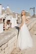 © Татьяна Волкова - Vertical pretty woman, bride in white festive wedding lace dress stand, posing near center of Italy with house and sky