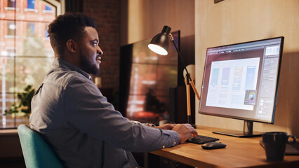 Young Handsome African American Man Working from Home on Desktop Computer in Sunny Stylish Loft Apartment. Creative Male Checking Social Media, Browsing Internet. Urban City View from Big Window.