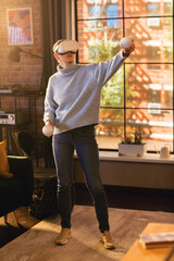 Wall Mural - Vertical Screen: Young Female Gamer with Short Hair Having Fun and Playing Virtual Reality Game at Home in Her Living Room. She is Wearing a Modern Headset and Using Controllers.