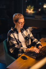 Fototapete - Vertical Screen: Young Attractive Woman Using Laptop Computer in Stylish Loft Apartment in the Evening. Creative Female Checking Social Media, Browsing Internet, Wearing Cozy Clothes.