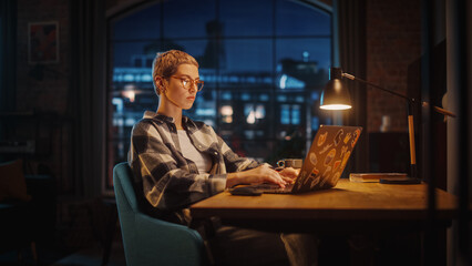 Fototapete - Young Woman Using Laptop Computer in Stylish Loft Apartment in the Evening. Tired Female Checking Social Media, Browsing Internet while Feeling Sleepy. Urban City View from Big Window.