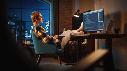 Aufkleber - Young Woman Writing Code on Computer in Stylish Loft Apartment in the Evening. Creative Female Wearing Cozy Clothes, Resting Feet on Table and Using Wireless Keyboard. Urban City View from Big Window.