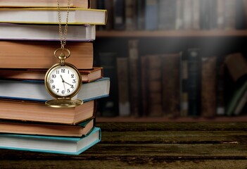 Wall Mural - old clock on a chain with stack books on library background. retro clock as a symbol of time a books