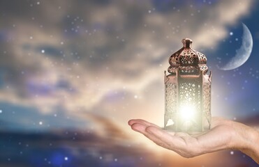 Wall Mural - Ornamental Arabic Muslim lantern with burning candle glowing in hand on night background