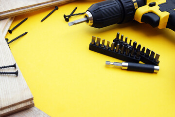 Yellow-black screwdriver on a yellow background, screws, a set of bits.